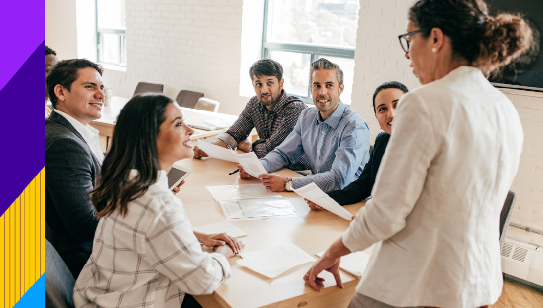 Men and women sitting at desk smiling at a women standing up
