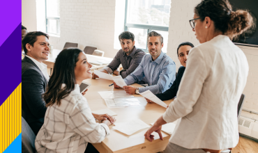Men and women sitting at desk smiling at a women standing up